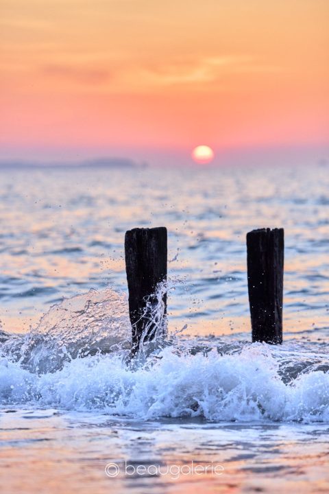 Coucher de soleil à Saint-Malo avec une vague figée contre deux pieux