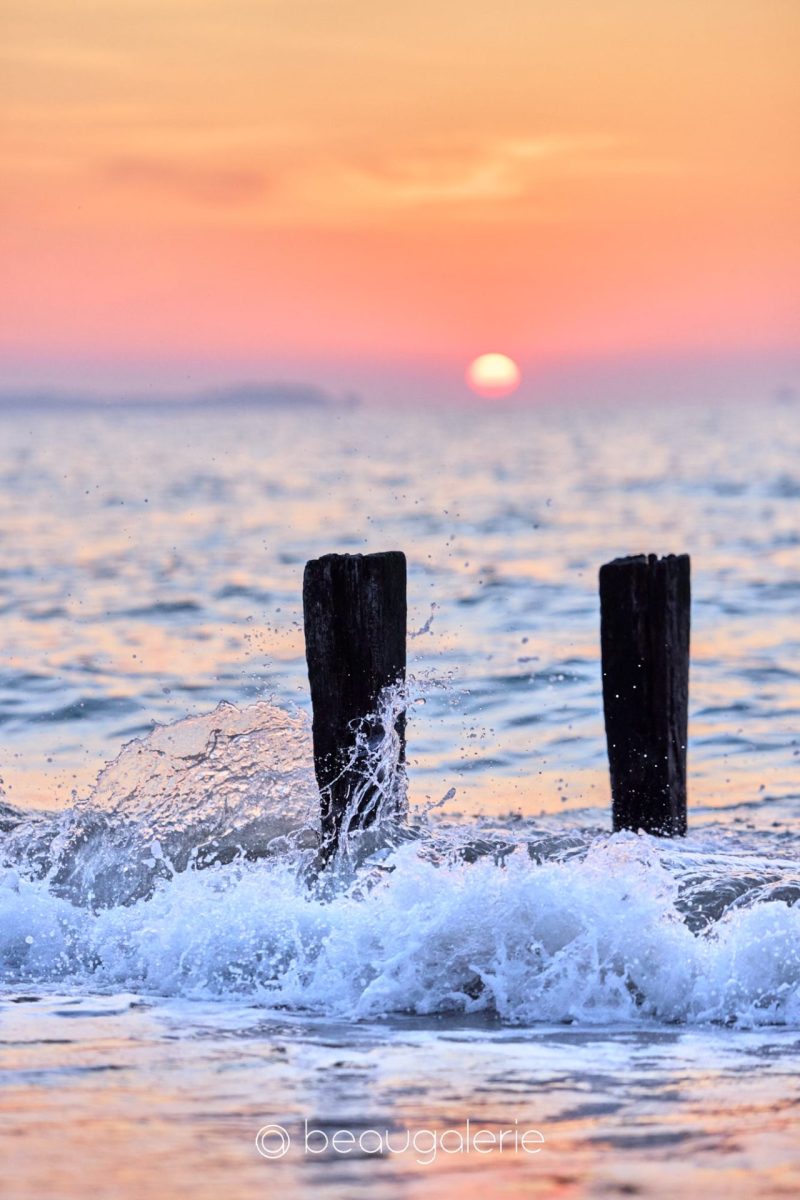 Coucher de soleil à Saint-Malo avec une vague figée contre deux pieux