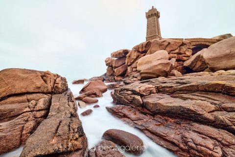 Photographie d'art montrant le granit rose sous les nuages avec le phare de Ploumanac'h en Bretagne.