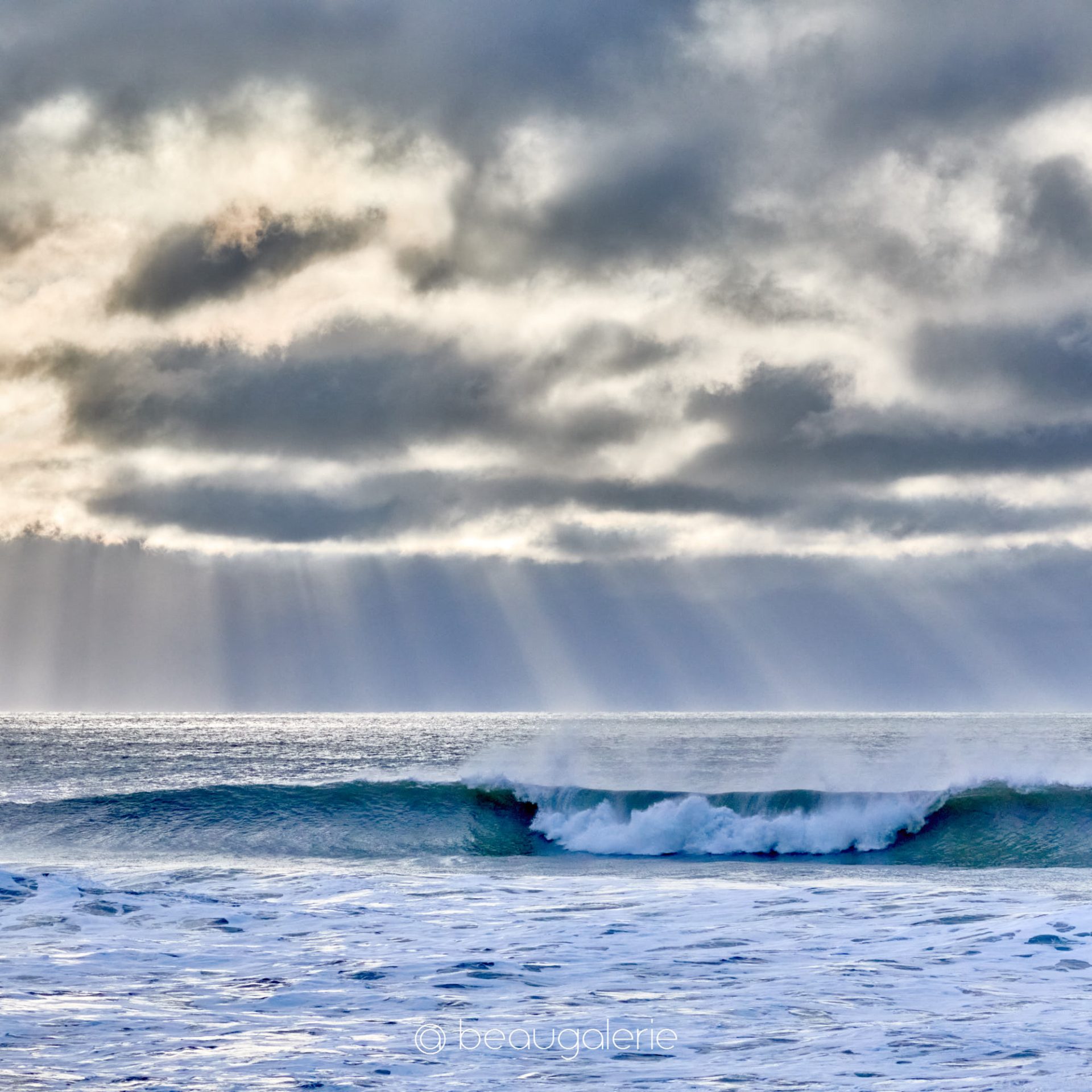 vague-lumiere-divine-quiberon Vague puissante déferlant sur la Côte Sauvage de Quiberon sous des rayons de lumière divine perçant les nuages.