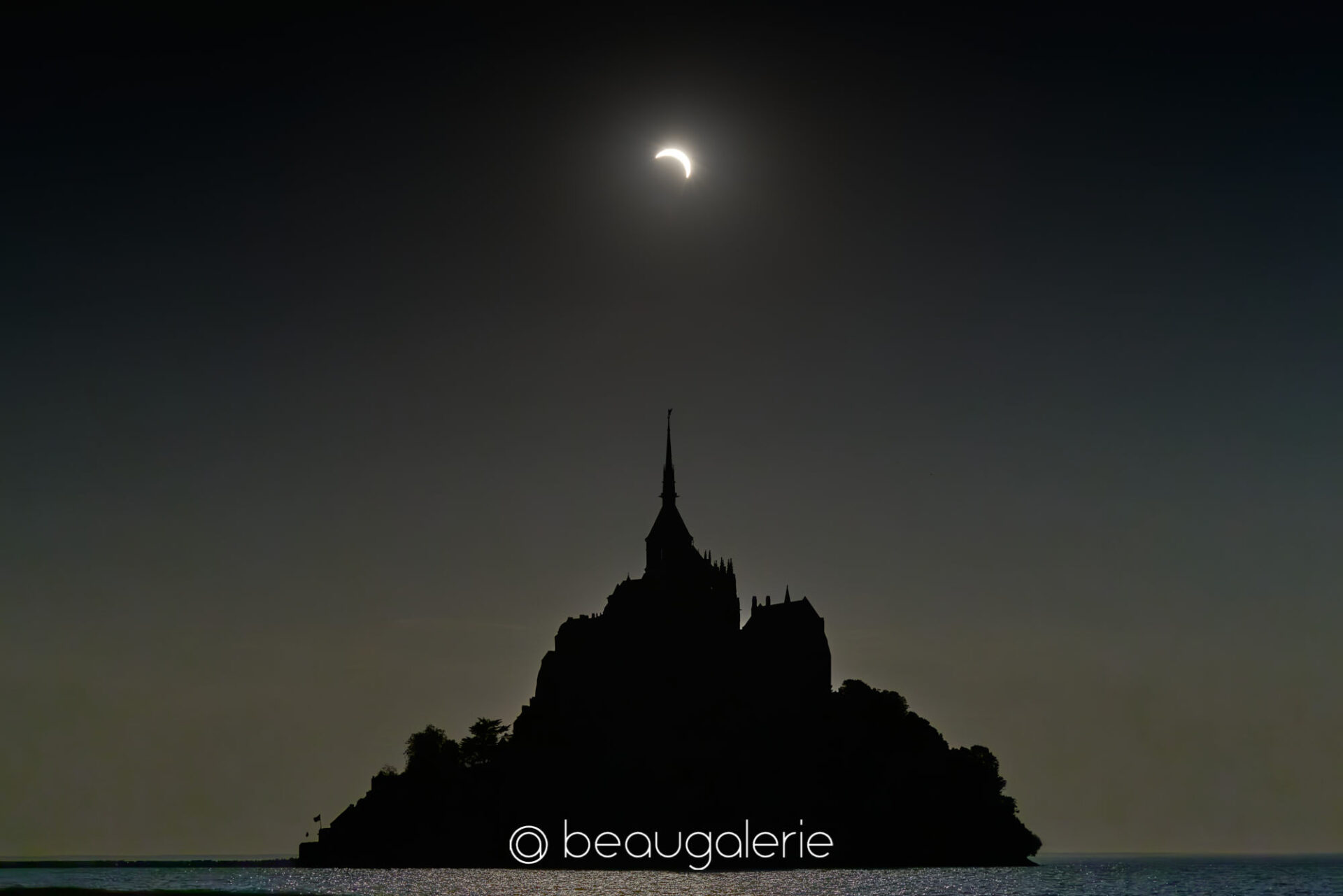 Eclipse solaire rare dans le ciel de la baie du Mont Saint-Michel Eclipse solaire baie Mont Saint-Michel, croissant lumineux au-dessus de la silhouette du mont, format standard, photographie d'art