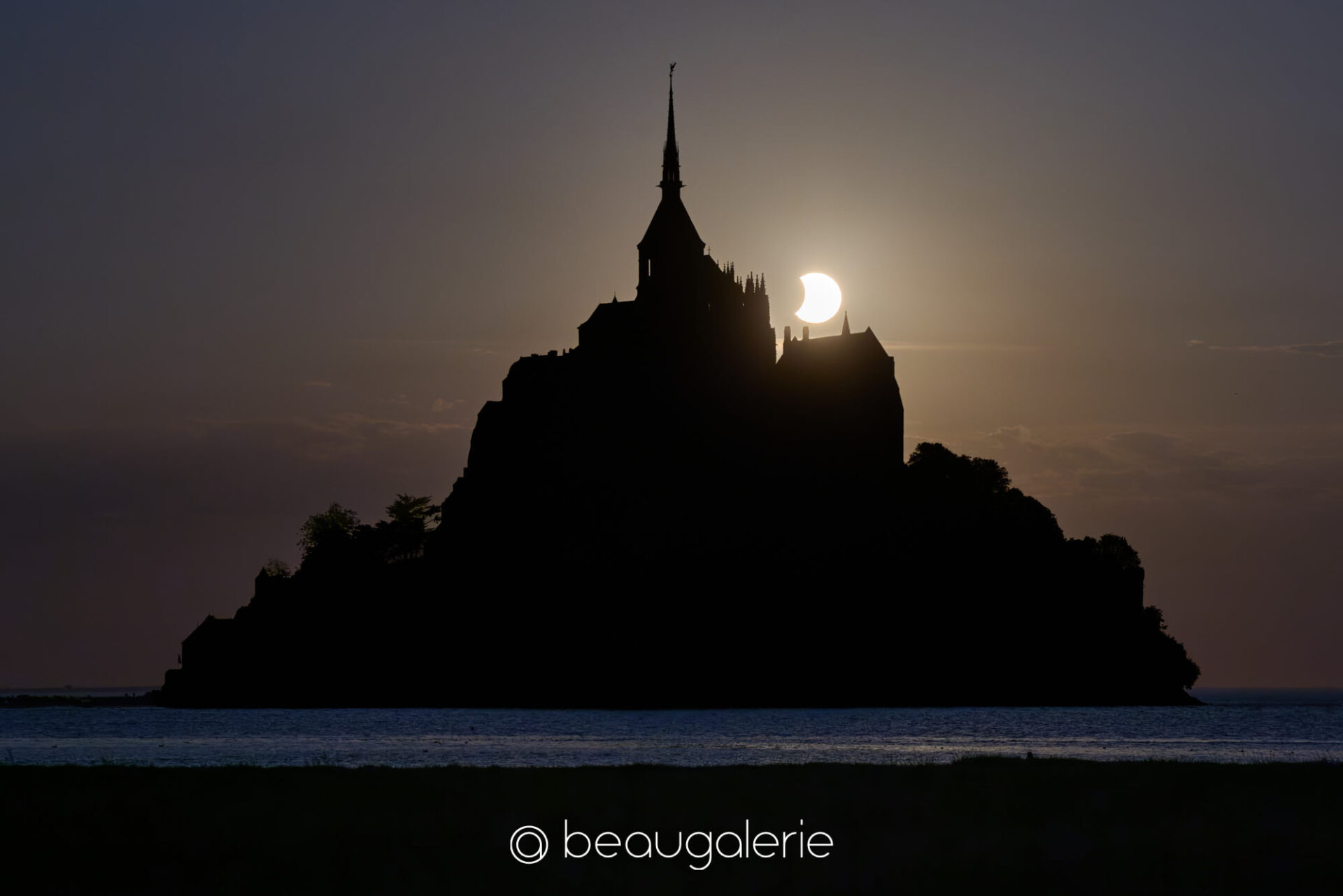 La fin de l'éclipse au Mont Saint-Michel La fin de l'éclipse au Mont Saint-Michel, disque solaire partiellement voilé derrière les tourelles de l'abbaye, format standard, photographie d'art